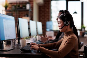 A female agent wearing a headset and working at a desktop computer in a modern office