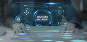 Person typing on a computer keyboard with a futuristic digital overlay displaying "Disaster Recovery" and IT icons
