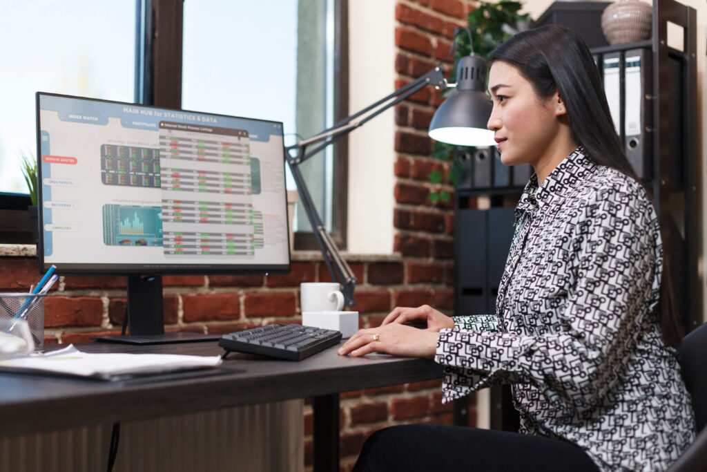 A woman sitting at a desk monitoring data on a desktop computer screen