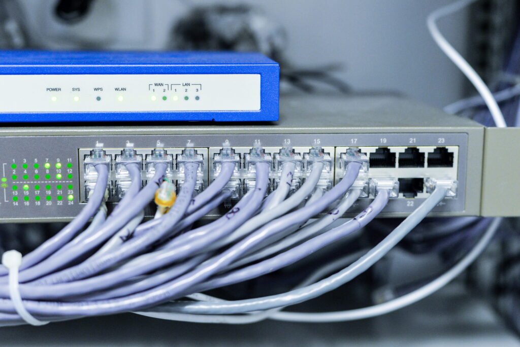 A network switch with multiple plugged-in Ethernet cables and glowing green indicator lights