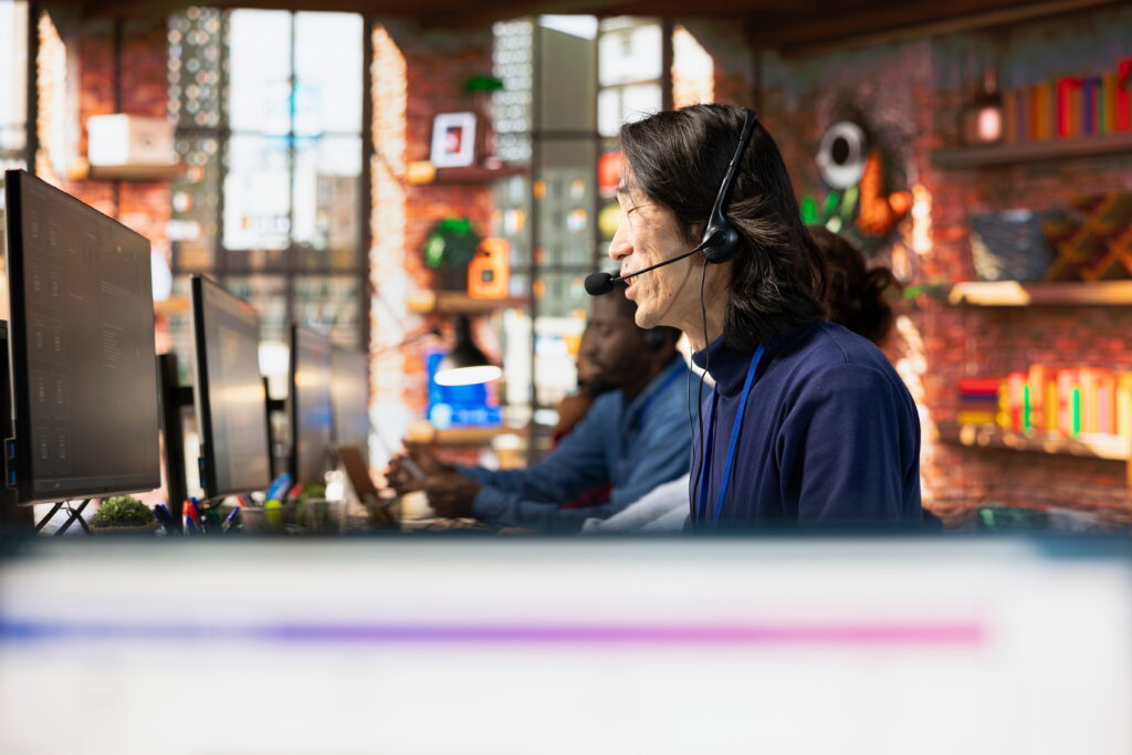 A customer support agent wearing a headset smiles while working at a computer in a modern office