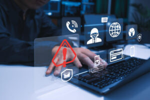 A person typing on a laptop with overlay icons depicting cybersecurity threats, a red warning triangle, and digital security features.