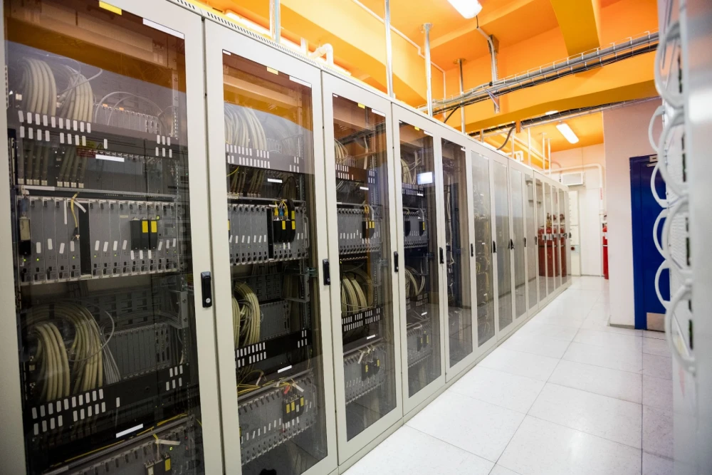 A row of glass doored server cabinets filled with neatly organized cables in a brightly lit data center room.