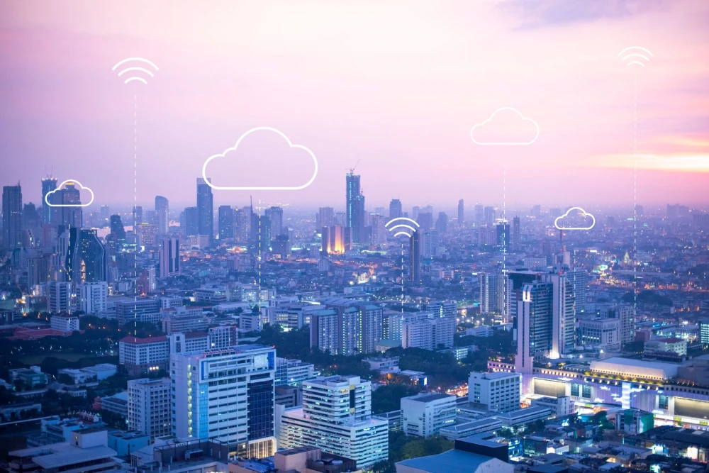 High angle view of a city skyline at dusk with white cloud computing and Wi Fi graphic overlays.