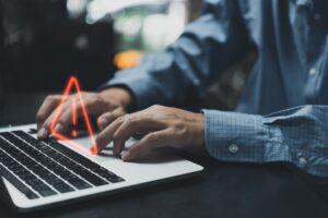 Close-up of a person typing on a laptop with a glowing red warning triangle icon overlaid near the trackpad.